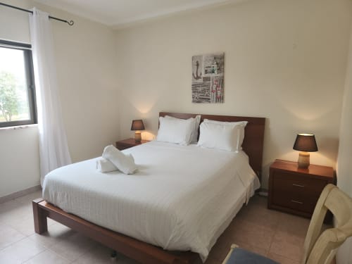 Quarto duplo ensolarado no Sunny House hostel em Lagos com roupas de cama brancas, móveis de madeira escura e vista para a cidade