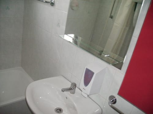 Banheiro compartilhado na pousada Sunny House em Lagos com pia branca, espelho, dispensador de sabonete e paredes azuleijadas