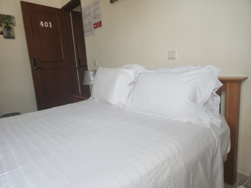 Lit double propre avec draps blancs dans la chambre 401 de l'auberge Sunny House, Lagos