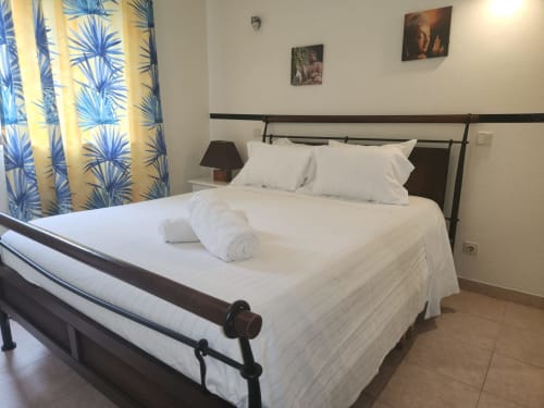 Chambre double économique à la Sunny House auberge de Lagos avec literie blanche, lit à structure métallique noire et rideaux bleu à motifs