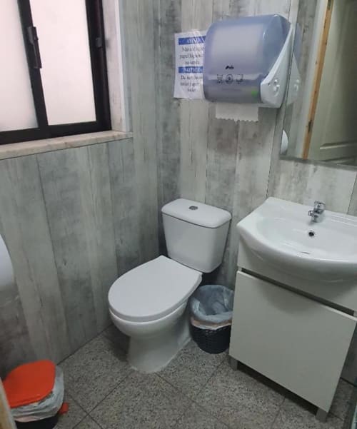Salle de bains commune de l'auberge Sunny House à Lagos avec toilettes, lavabo, distributeur d'essuie-mains et panneau d'affichage