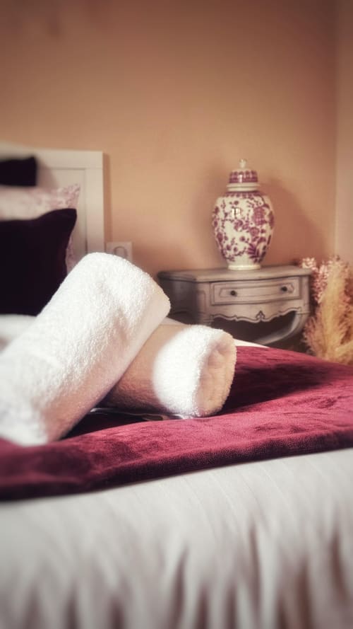 Serviettes blanches roulées sur la literie bordeaux du Manoir Le Coutureau avec un pot à gingembre décoratif sur la table de nuit