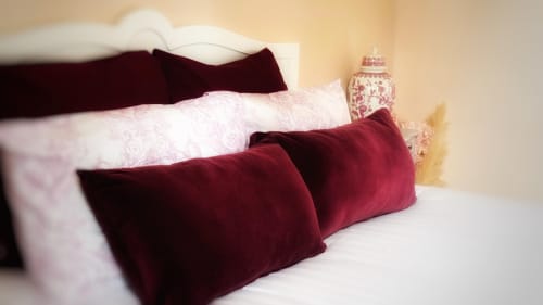 Chambre élégante au Manoir Le Coutureau avec coussins en velours bordeaux, draps blancs et accessoires décoratifs sur la table de nuit