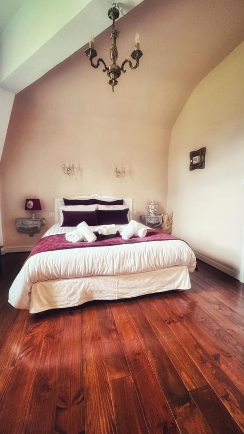 Chambre élégante au Manoir Le Coutureau avec plafond voûté, literie bordeaux, parquet et lustre raffiné