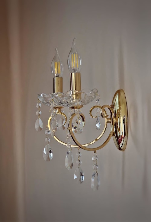 Élégant lustre en cristal aux bras en laiton doré et ampoules LED bougie dans la chambre du Manoir Le Coutureau