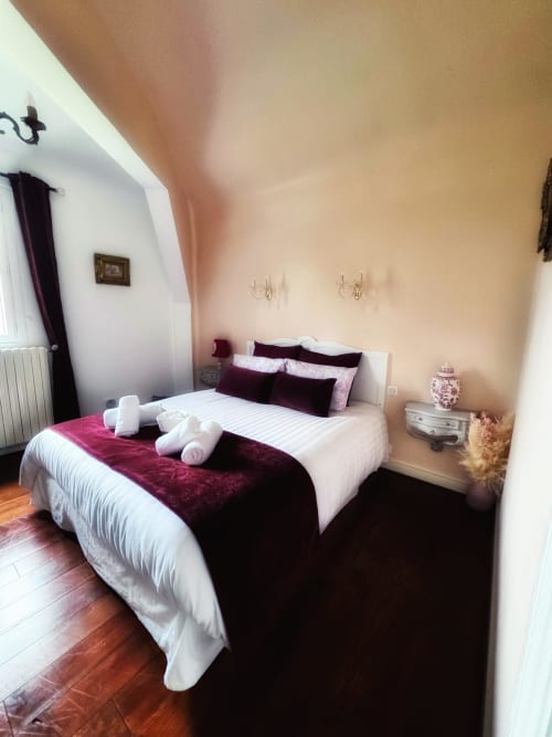 Chambre élégante du Manoir Le Coutureau avec literie bordeaux et blanche, serviettes roulées, murs crème et parquet
