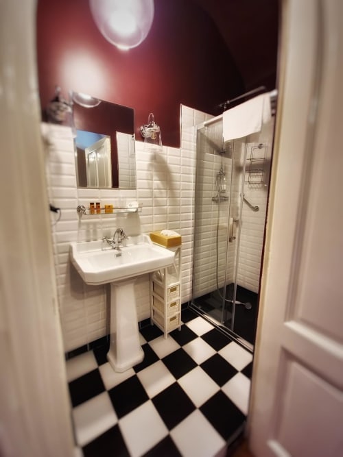 Salle de bain moderne au Manoir Le Coutureau avec sol à carreaux noir et blanc, murs en carrelage blanc, lavabo sur colonne, et