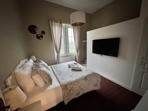 Chambre moderne au Manoir Le Coutureau avec lit, TV écran plat, lampe suspendue et vue sur la fenêtre à Rouffignac de Sigoules