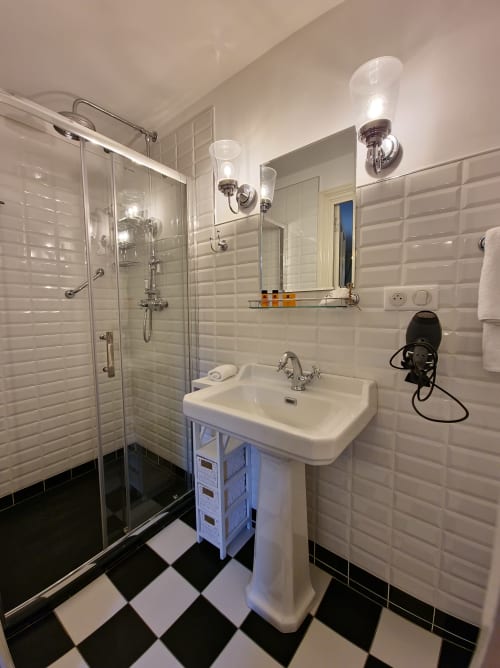 Salle de bains moderne du Manoir Le Coutureau avec carrelage métro blanc, lavabo sur colonne, douche vitrée et style noir et blanc
