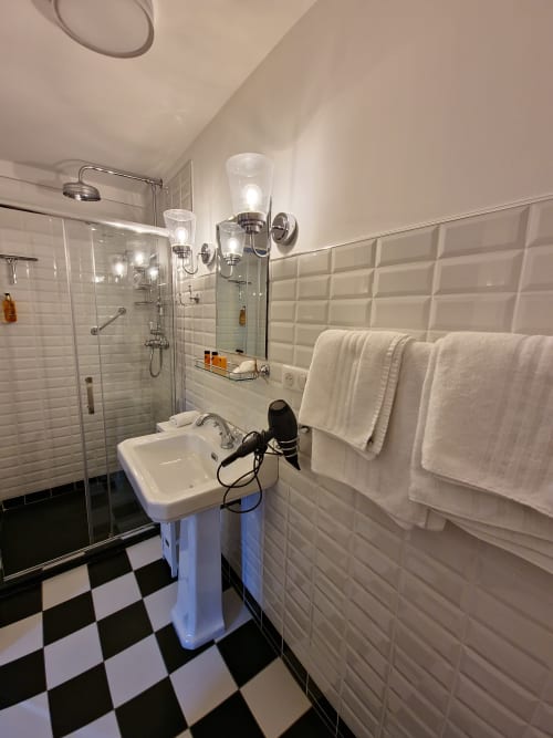 Salle de bains moderne du Manoir Le Coutureau avec carrelage noir et blanc, douche à l'italienne, lavabo sur colonne et serviettes moelleuses