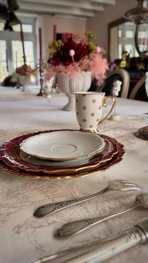 Mise de table élégante au Manoir Le Coutureau avec assiette de présentation bordeaux, tasse à pois et composition florale fraîche