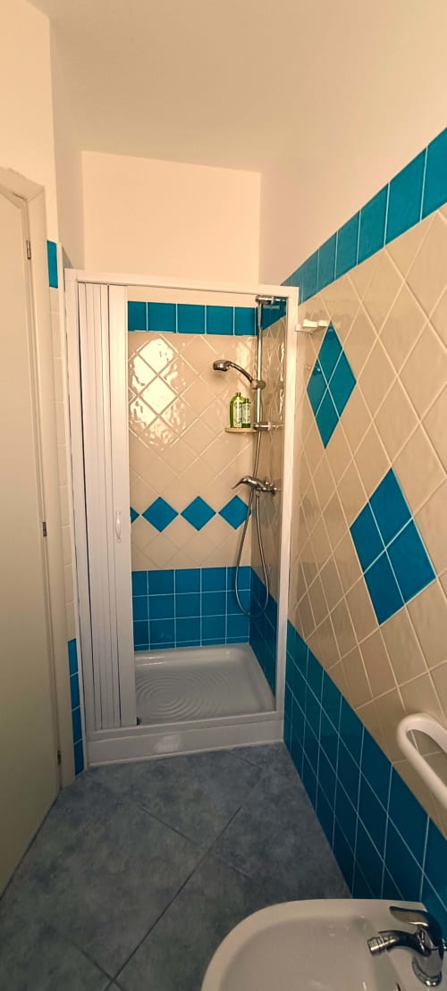 Bagno moderno con piastrelle a rombi blu e crema, doccia a filo pavimento e vista mare dell'appartamento Panoramici Monolocali