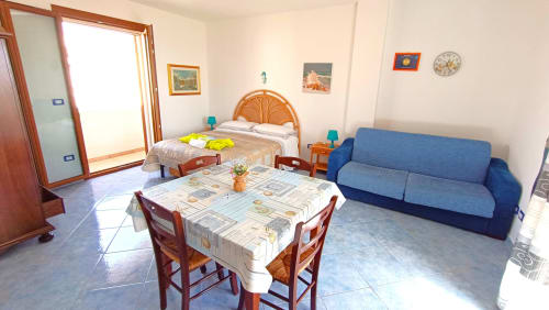 Monolocale panoramico a Leuca con zona pranzo, divano blu, letto in legno e vista mare dal balcone