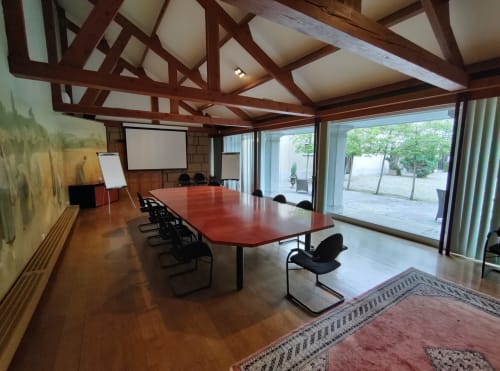Salle de conférence moderne au Château d'Hassonville avec table rouge, poutres apparentes et vue sur les jardins à Marche-en-Famenne
