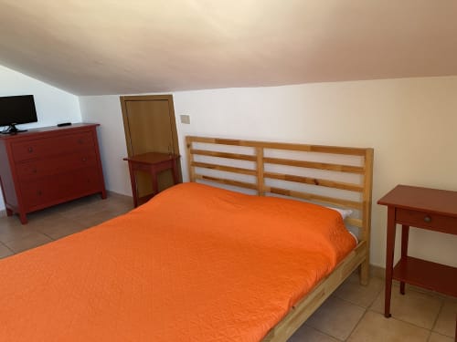Luminosa camera da letto con letto in legno, biancheria arancione, mobili rossi e vista sulle montagne a Rigiariloo Home Apartments a San