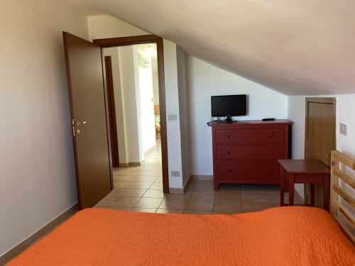 Camera spaziosa nell'appartamento Rigiariloo Home Apartments a San Giacomo degli Schiavoni con biancheria arancione, cassettiera rossa e