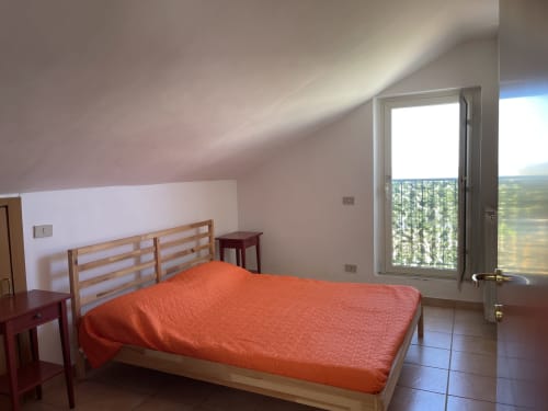 Luminosa camera da letto in mansarda presso Rigiariloo Home Apartments con biancheria arancione, letto in legno e vista montagne
