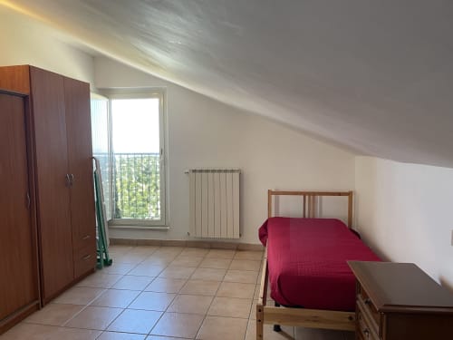 Camera da letto luminosa in mansarda con vista sulle montagne, armadio in legno, letto rosso e riscaldamento a radiatori.