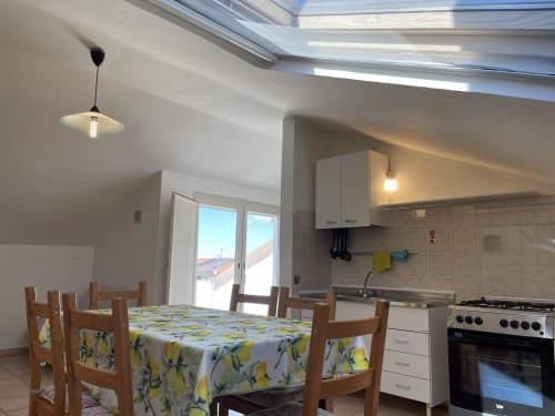 Luminosa zona cucina-pranzo con sedie in legno, tovaglia a limoni, lucernario e viste montane agli Apartamenti Rigiariloo Home