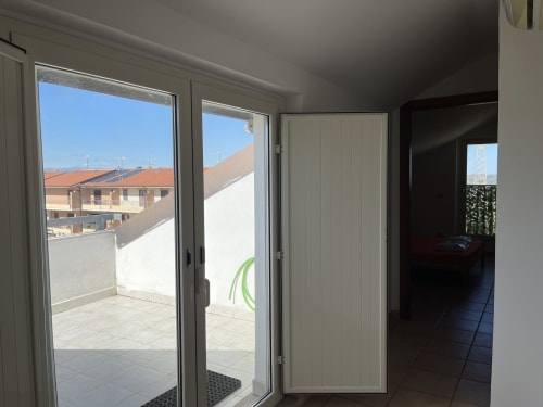 Luminoso interno dell'appartamento a Rigiariloo Home con porte-finestre affacciate su tetti e montagne vicino a San Giacomo degli