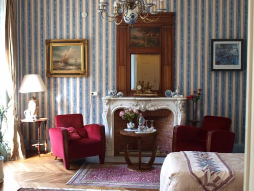 Chambre élégante à la Villa Magnolia Parc avec fauteuils en velours rouge, cheminée, papier peint rayé et vue sur le jardin à Montélimar