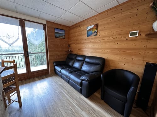 Salon de charme aux Gîtes Des Planchettes : canapé en cuir noir, boiseries, vue panoramique depuis le balcon