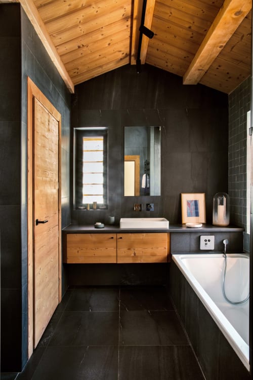 Salle de bains moderne au Chalet Mont-Blanc avec murs noirs, poutres en bois au plafond, meuble-lavabo en bois et baignoire blanche