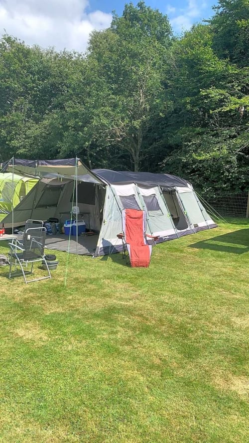 Camping tent setup at Postwood Gardens Campsite in Kentisbeare with green lawn and forest backdrop