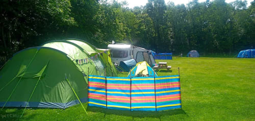 Green tent and colorful windbreak at Postwood Gardens Campsite in Kentisbeare with lush grass and woodland