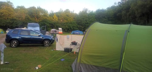 Camping setup at Postwood Gardens Campsite in Kentisbeare with green tents, parked car, and wooded surroundings