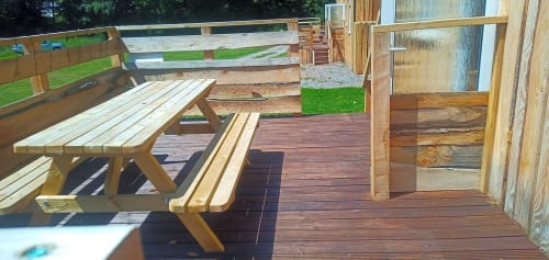 Wooden picnic tables and benches on a deck at Postwood Gardens Campsite in Kentisbeare with green grounds and wooden
