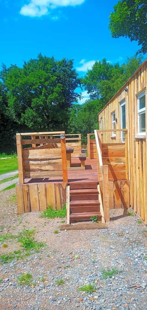 Wooden cabin entrance at Postwood Gardens Campsite in Kentisbeare with deck stairs and green countryside surroundings