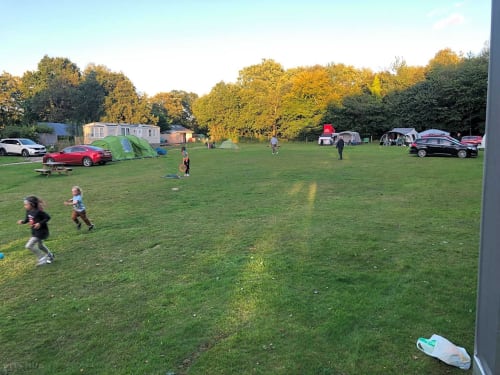 Families camping at Postwood Gardens Campsite in Kentisbeare with tents, caravans, and children playing on green grounds at