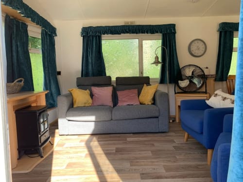 Cozy interior at Postwood Gardens Campsite with gray sofa, colorful pillows, wooden furniture, and large windows overlooking