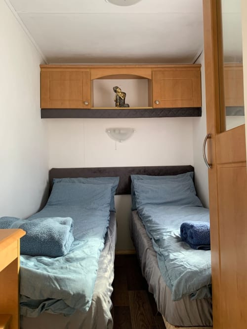 Twin bedroom with blue bedding at Postwood Gardens Campsite, Kentisbeare. Wooden storage cabinets above beds with decorative