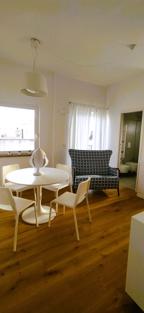 Moderno salotto a Bari con tavolo rotondo bianco, sedie in legno chiaro, poltrona decorata e finestre con vista mare