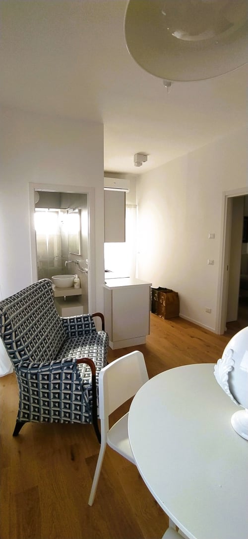 Zona living moderna dell'appartamento con angolo cottura, poltrona decorata e accesso al bagno presso Bari Vacation BnB