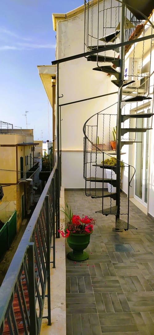 Terrazza sul tetto della B&B Bari Vacation con scala a spirale, fiori rossi e vista sul mare a Bari, Italia