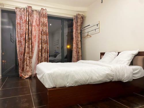 Chambre moderne à Chambre Pasteur à Montreuil : literie blanche, cadre bois foncé, rideaux à motifs rouges, carrelage sombre