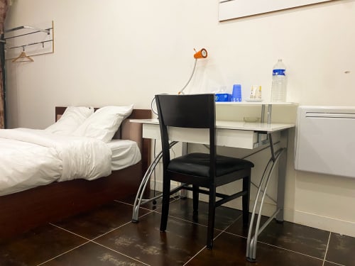 Chambre Pasteur de l'hôtel à Montreuil avec lit aux draps blancs, bureau avec chaise noire et équipements modernes