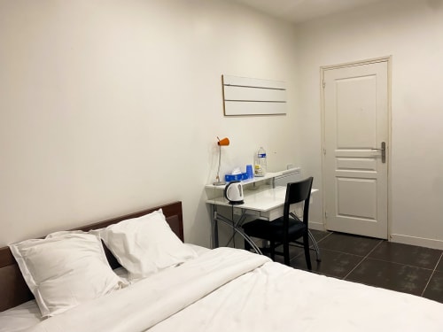 Chambre épurée et moderne à Chambre Pasteur Montreuil avec literie blanche, bureau de travail et porte.