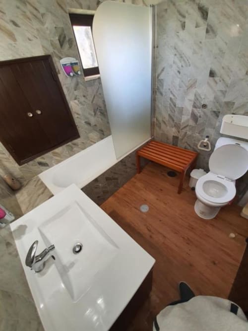 Ocean View Lagos hostel Economy Room shared bathroom with white sink, toilet, shower enclosure, wooden flooring, and tiled