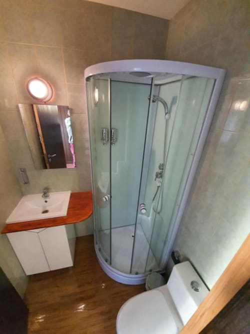 Modern shared bathroom at Ocean View Lagos hostel featuring curved glass shower enclosure, white sink with red countertop,