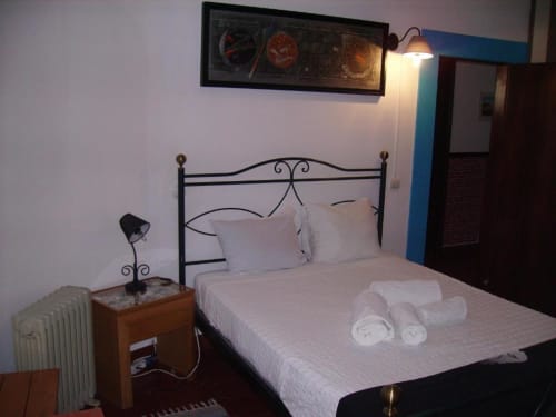 Habitación doble en el hostal Ocean View Lagos con cama de hierro forjado, sábanas blancas, mesilla de noche, lámpara y radiador.