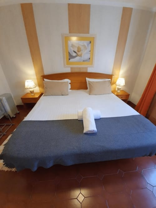 Habitación doble con cama de madera, ropa de cama blanca, manta azul, lámparas laterales y cuadros florales en el albergue Ocean View Lagos