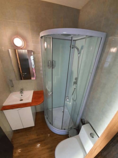 Baño moderno en el hostal Ocean View Lagos con ducha de esquina, lavabo blanco con encimera roja e inodoro