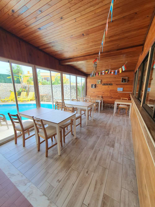 Wooden-ceiling dining room with tables and chairs overlooking pool at Ocean View Lagos hostel