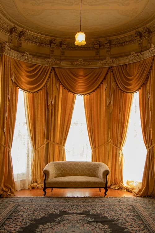 Élégant salon du Château De Brie avec rideaux dorés, causeuse vintage, plafond ouvragé et luminaires suspendus