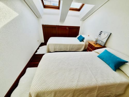 Dormitorio doble en apartamento Miudiño, Baiona con tragaluces, almohadas azules y muebles de madera