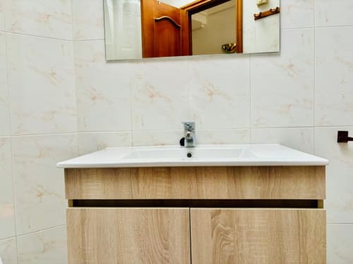 Vanidad de baño moderno con lavamanos blanco y mueblería de madera en apartamento de Baiona, hotel Holibai
